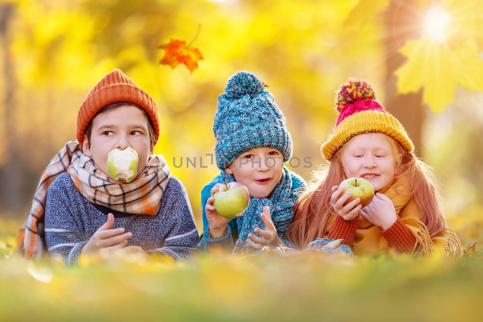 Children lying on the grass with apple in their hands in autumnal park. Beauty in fall natural garden.