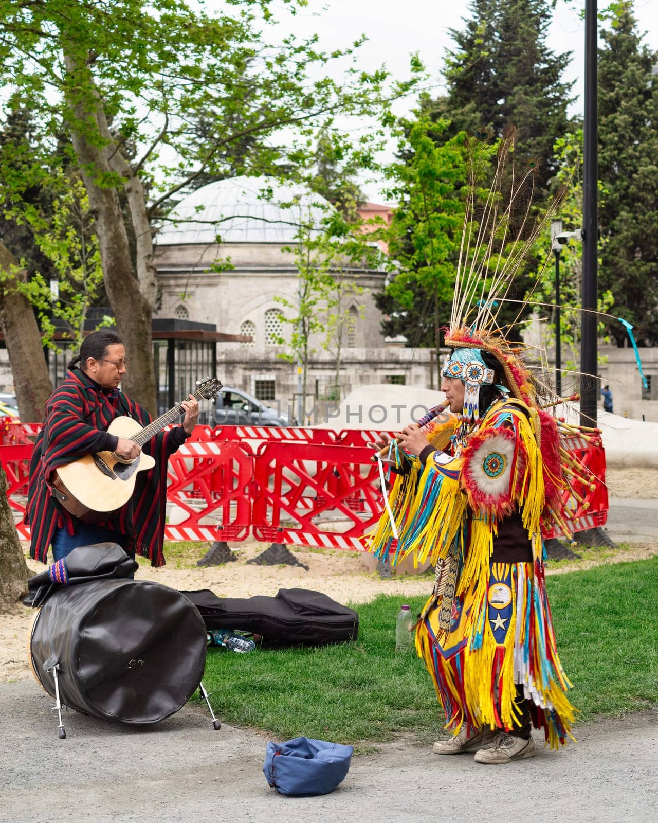 Istanbul, Turkey - May 5, 2023: Two Native Americans musicians wearing colorful traditional costume and busking playing courting flute and guitar in front of Kilic Ali Pasha Mosque in Karakoy