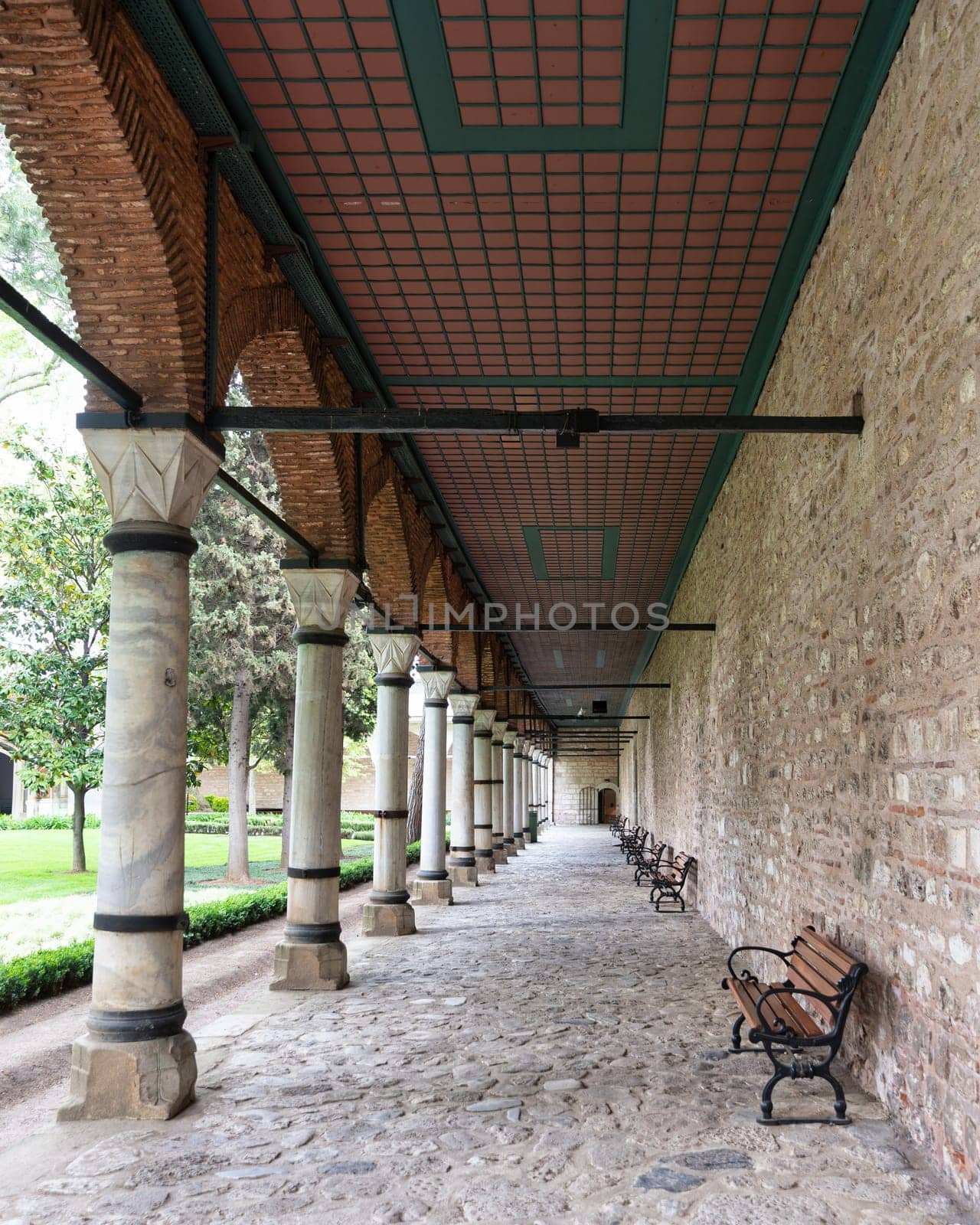 Long covered paved walkway with columns and benches. The walkway is located in the courtyard of Topkapi Palace, a former royal palace in Istanbul, Turkey