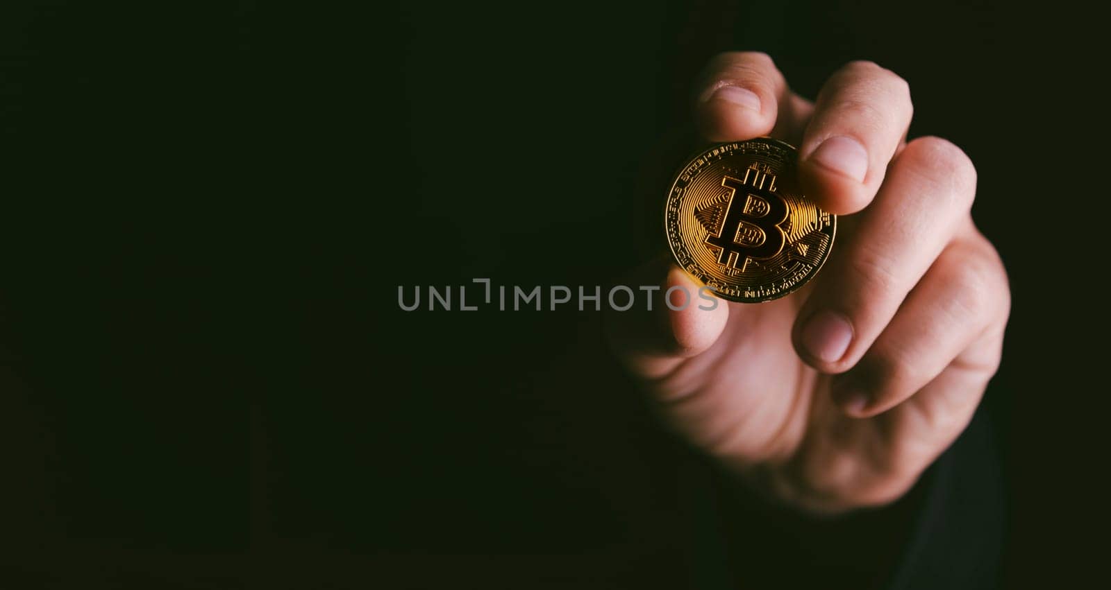 Closeup of golden bitcoin BTC cryptocurrency in hand over dark black background. Man holding golden crypto coin. Virtual money and blockchain concept.