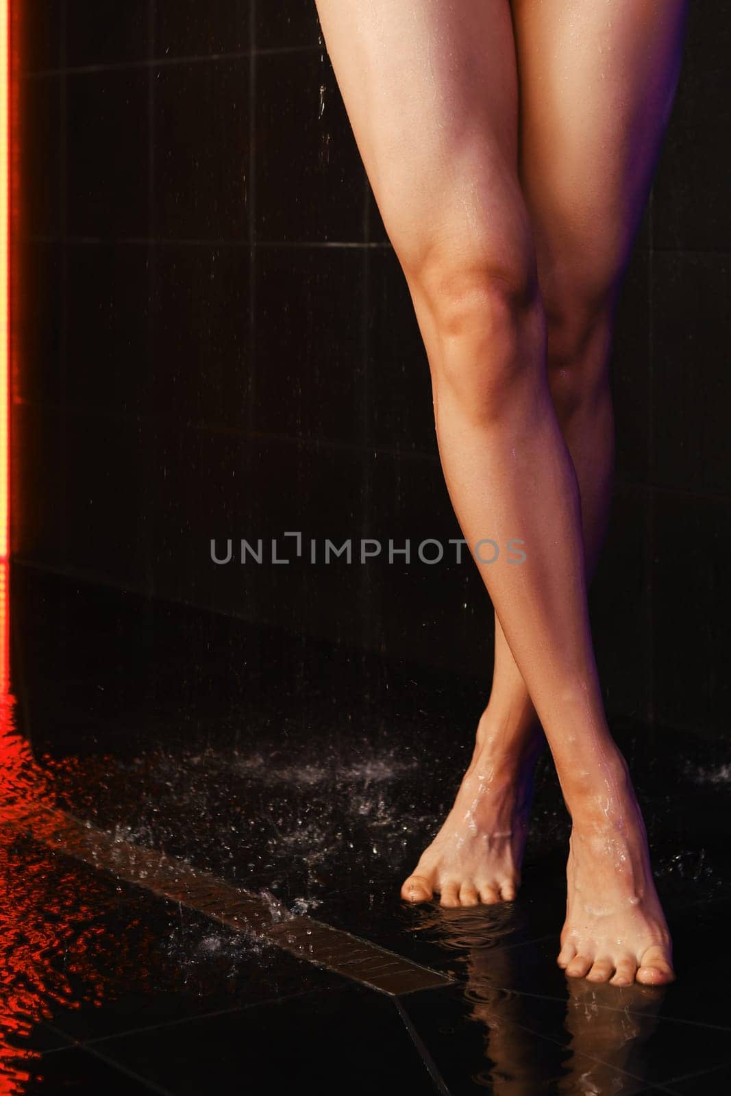 Crossed female legs in the shower with black tiles