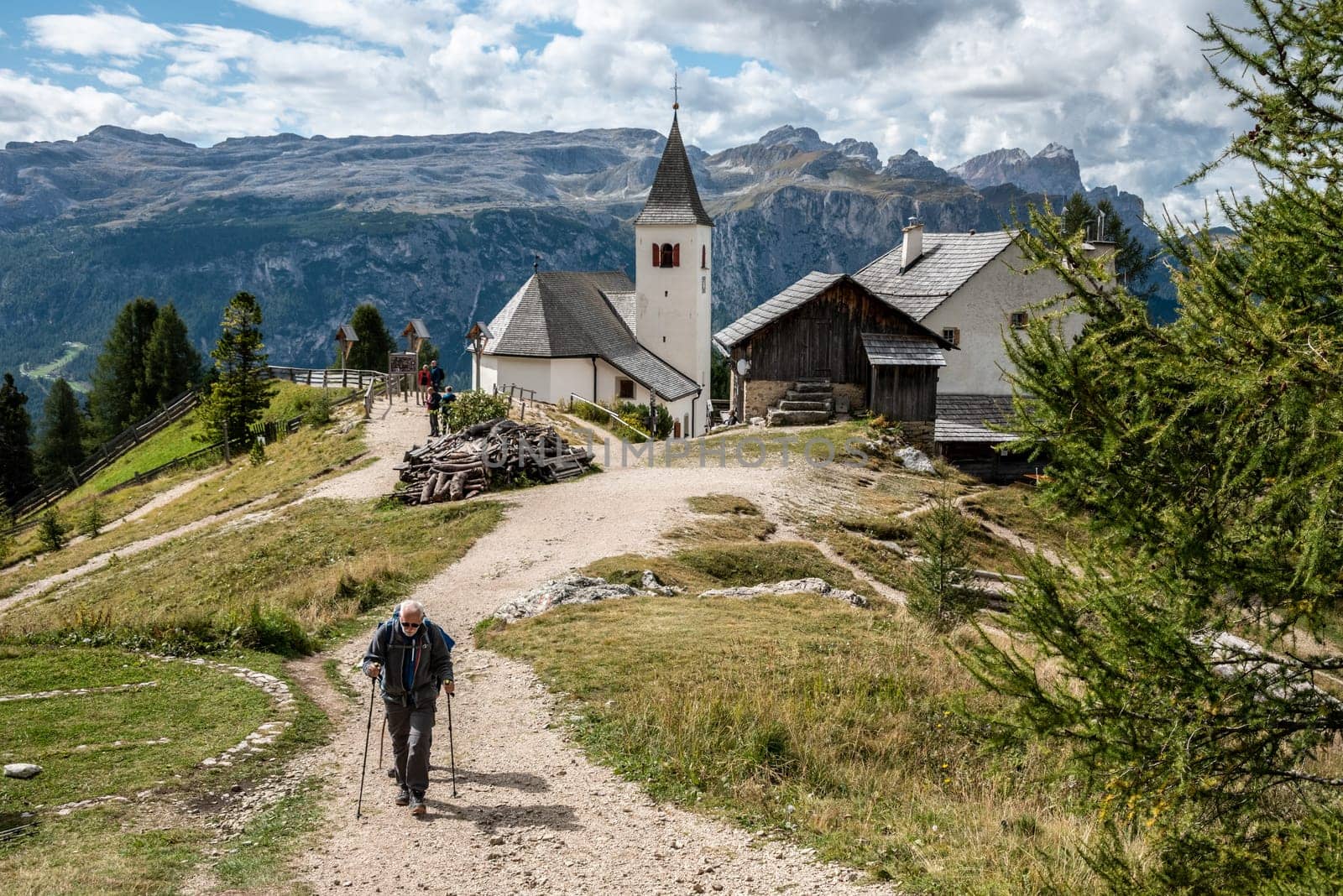 An elderly hiker in the Dolomite Alps, the Heilig Kreuz church in the background, South Tirol in Italy