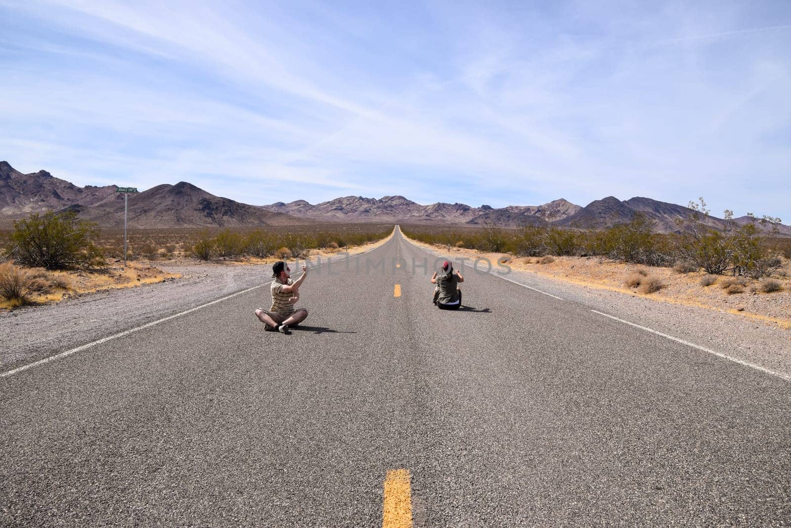 Two people pretending to drive on a highway in the Death Valley, USA