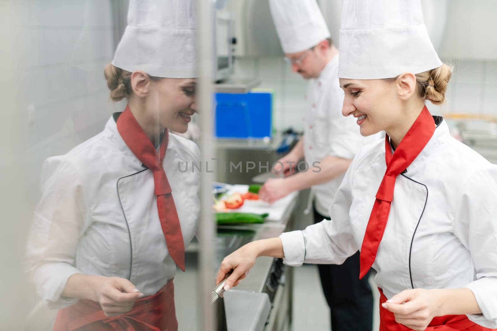 Chefs in large commercial kitchen cooking meals together stirring the sauce
