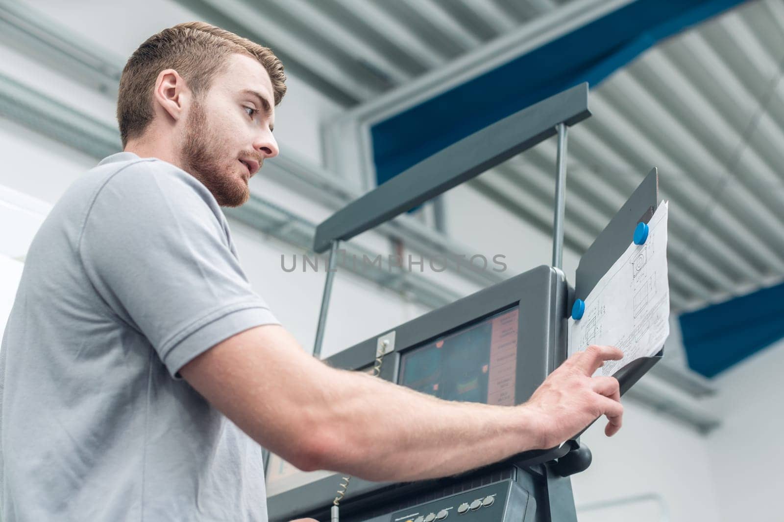 Worker in the metal industry entering data on screen of a modern machine tool in factory