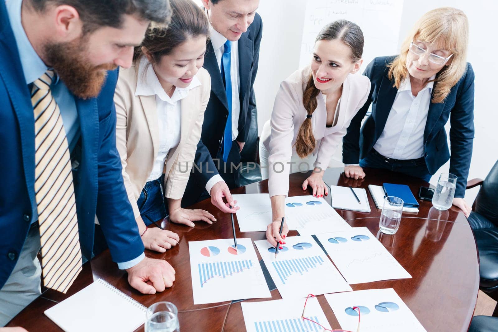 Multi-ethnic team of five dedicated specialists smiling while analyzing various charts with positive statistics about the profit and the development of the company