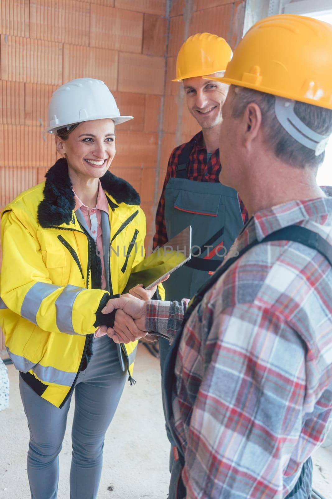 Smiling female contractor with tablet computer shaking hand of senior builder before starting work
