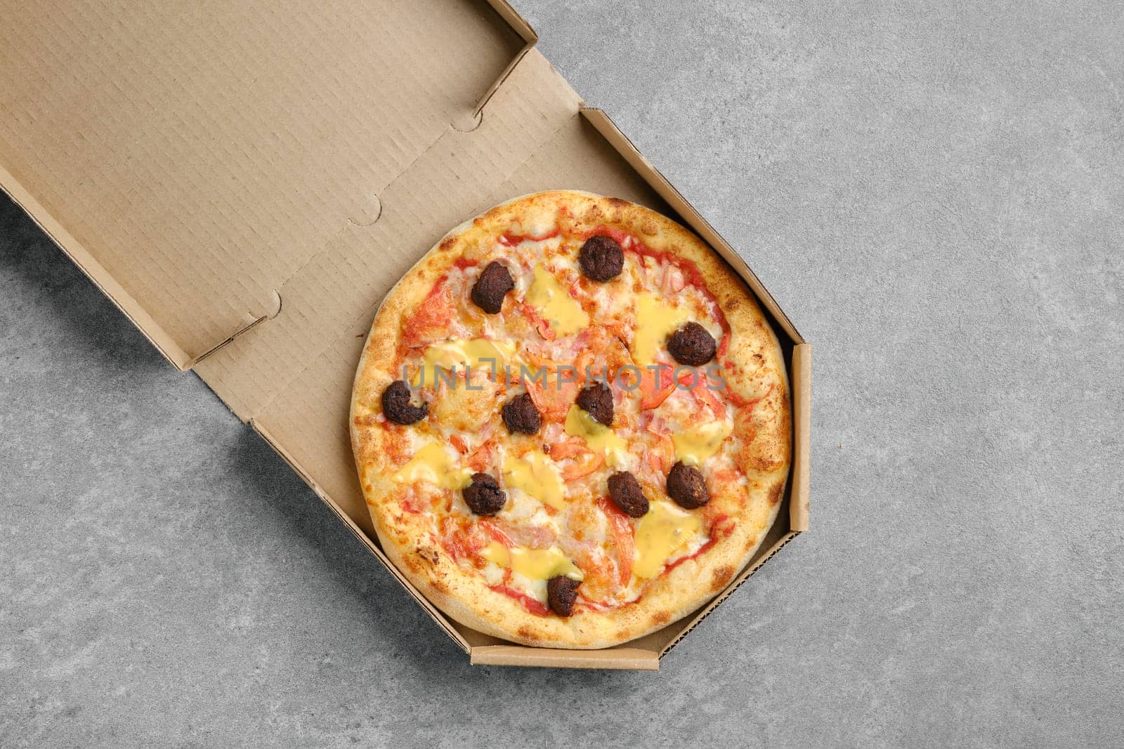 Top view of pizza with beef meatballs, cheddar and tomato slices in cardboard box