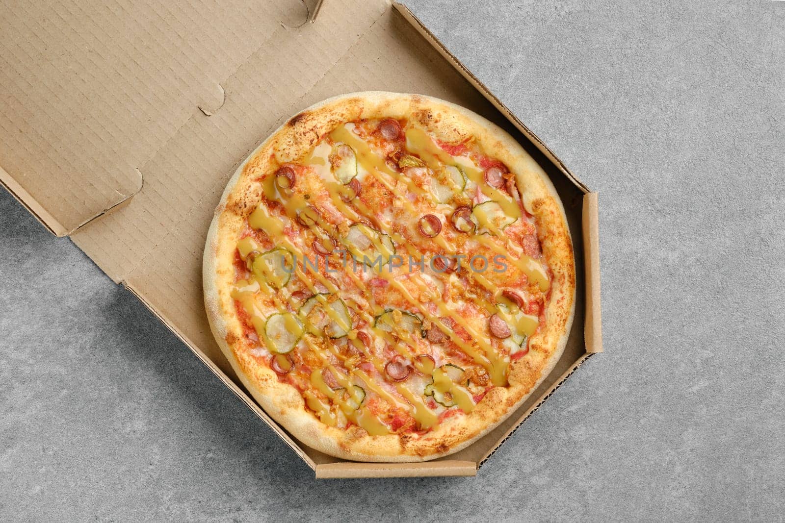 Top view of pizza with thin sausage and pickled cucumber in cardboard box