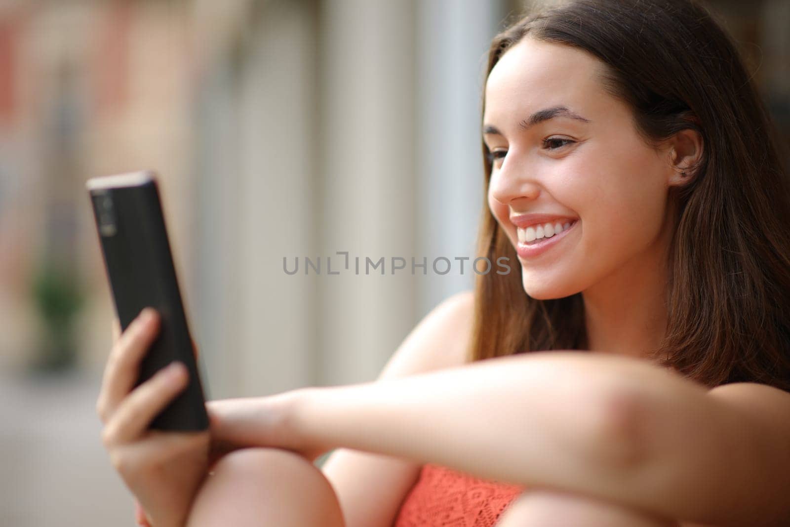Happy woman checking cellphone isitting n the street