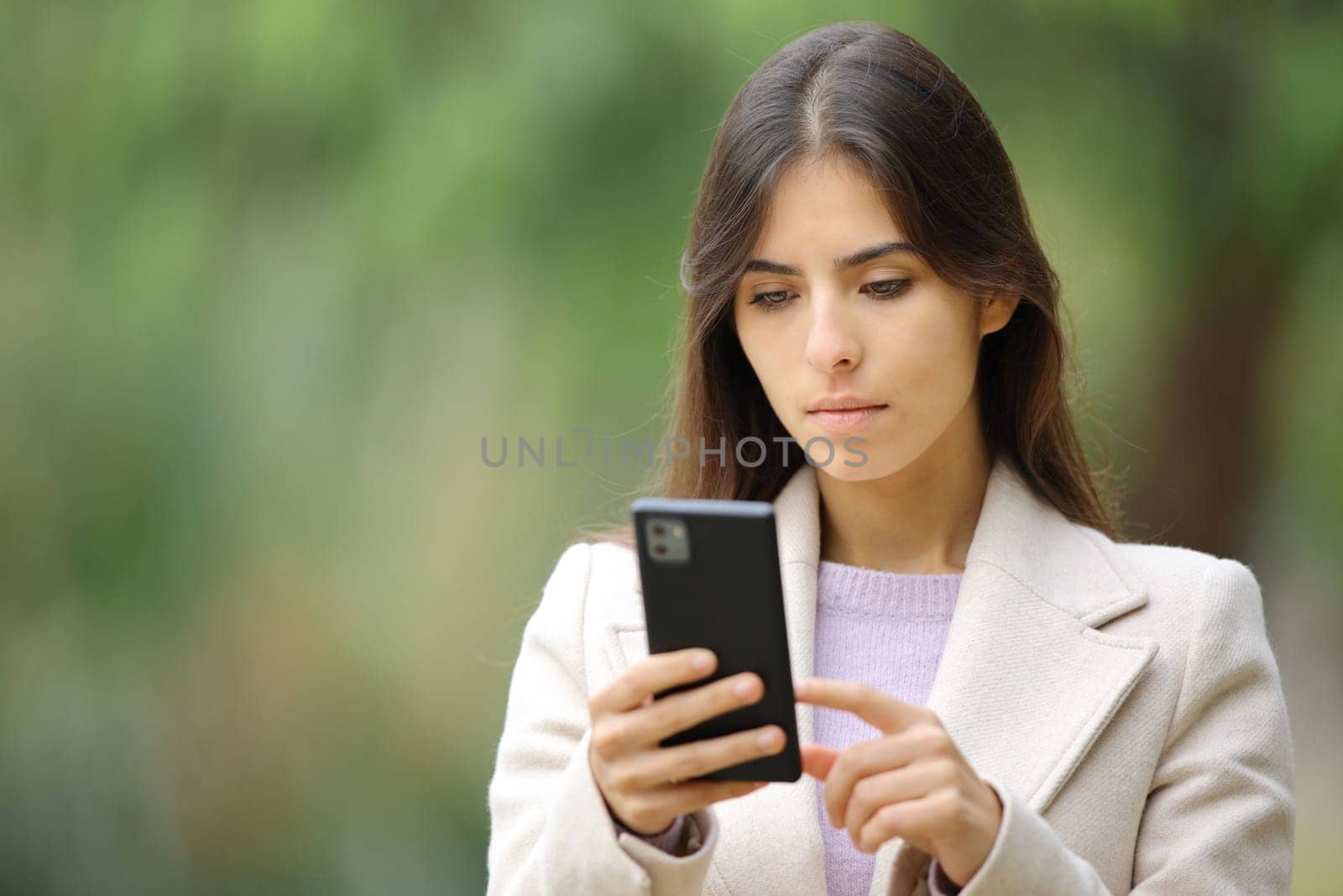 Serious woman using phone in winter outside walking in a park