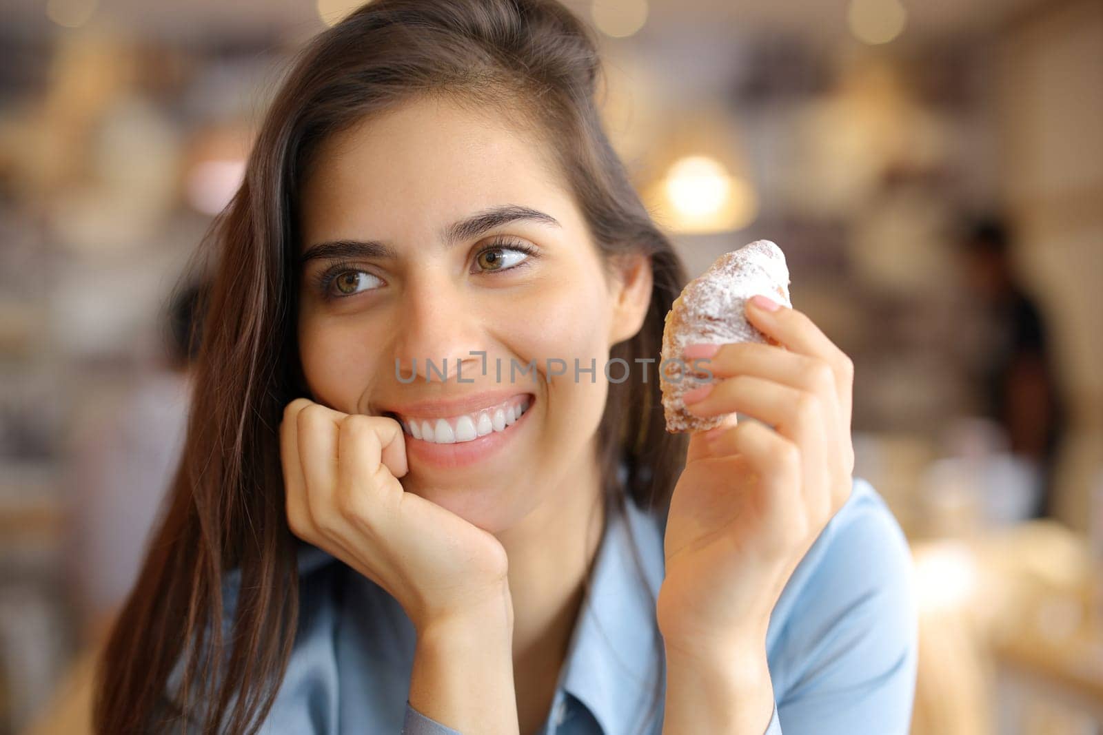 Happy woman with beauty smile holding croissant in a bar interior