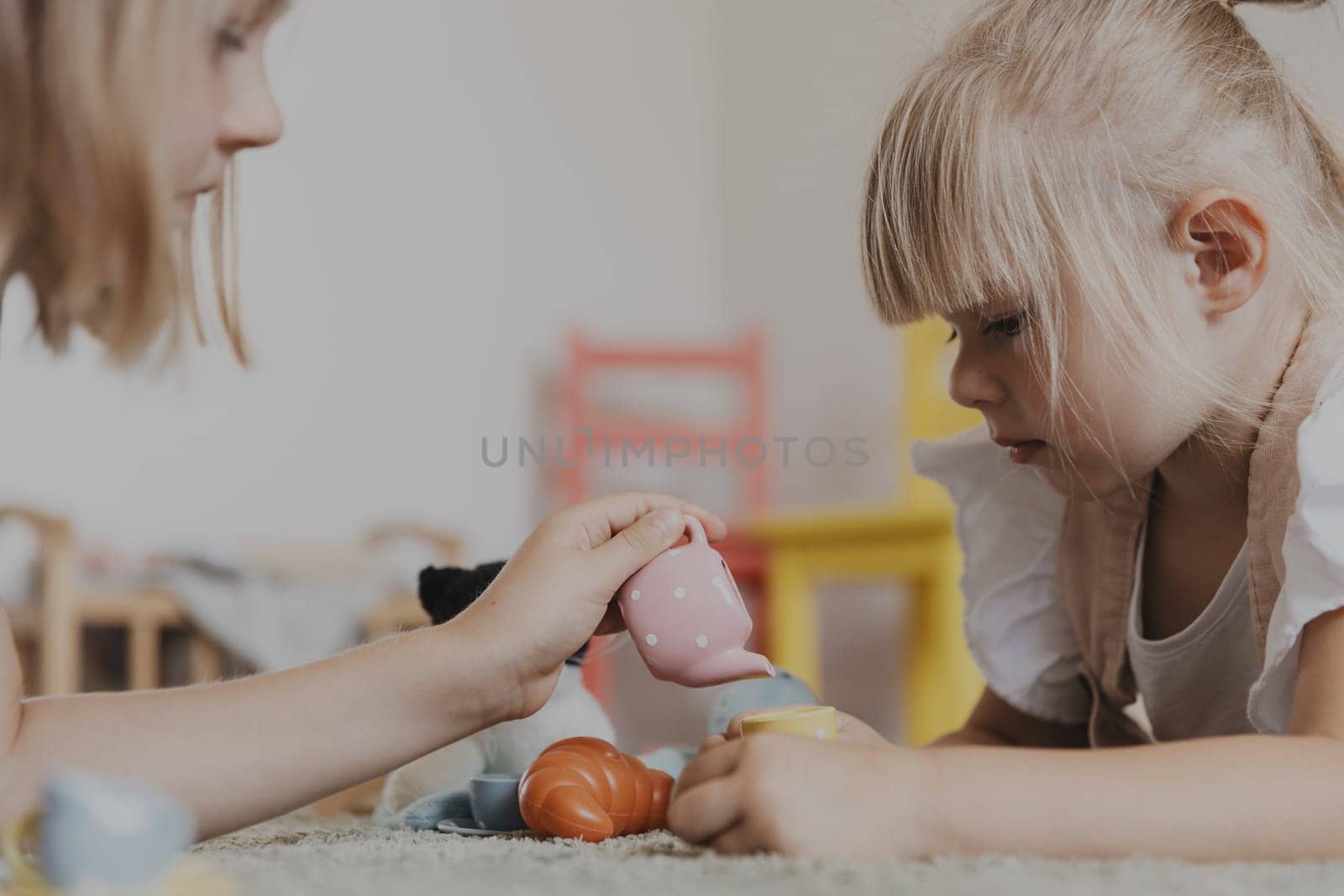 Close-up of female children playing with colorful toy kitchen play tea set. Kids lying on carpet at home bedroom, kindergarten. Educational eco-friendly games. Development of motor skills, imagination