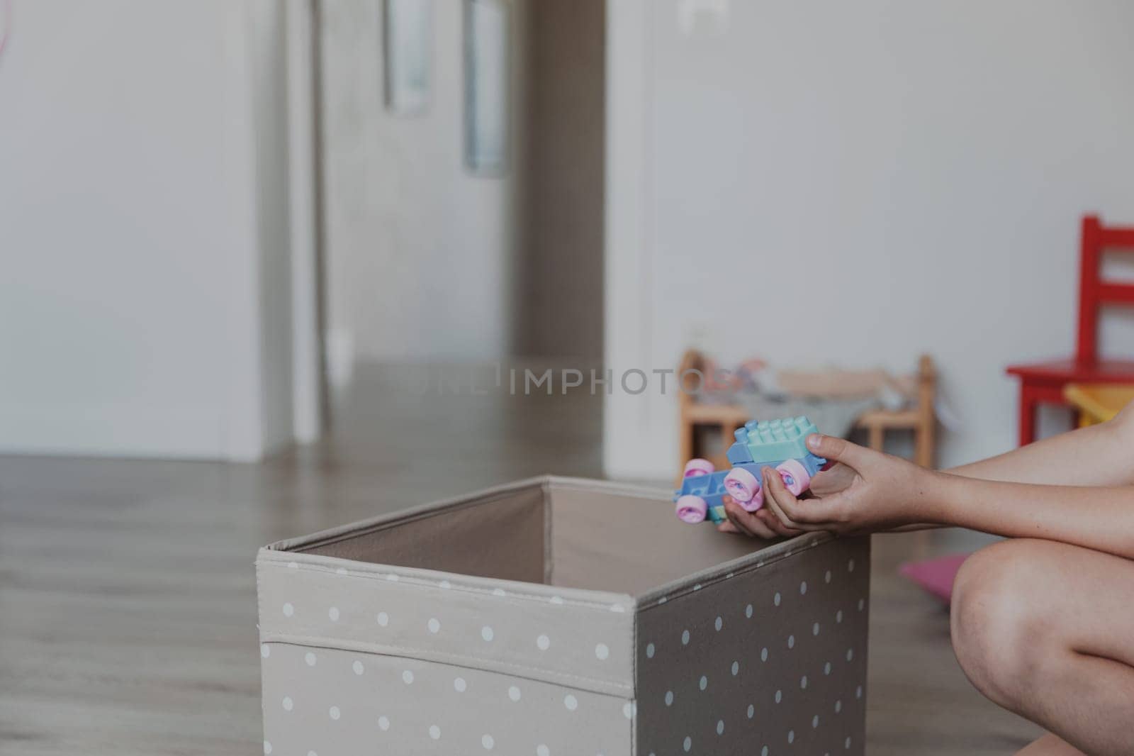 Child cleaning toys from floor after playing, collect them to textile box. Kid sitting on carpet at white home bedroom, kindergarten playroom or playground center. Educational eco-friendly games