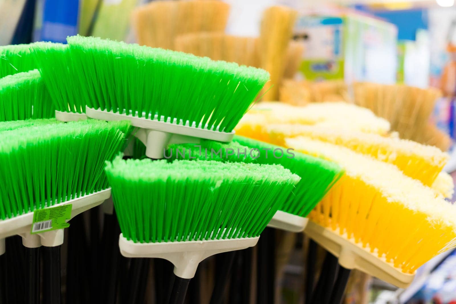 Plastic brushes for cleaning premises. Assortment of multi-colored brooms in store. Close-up