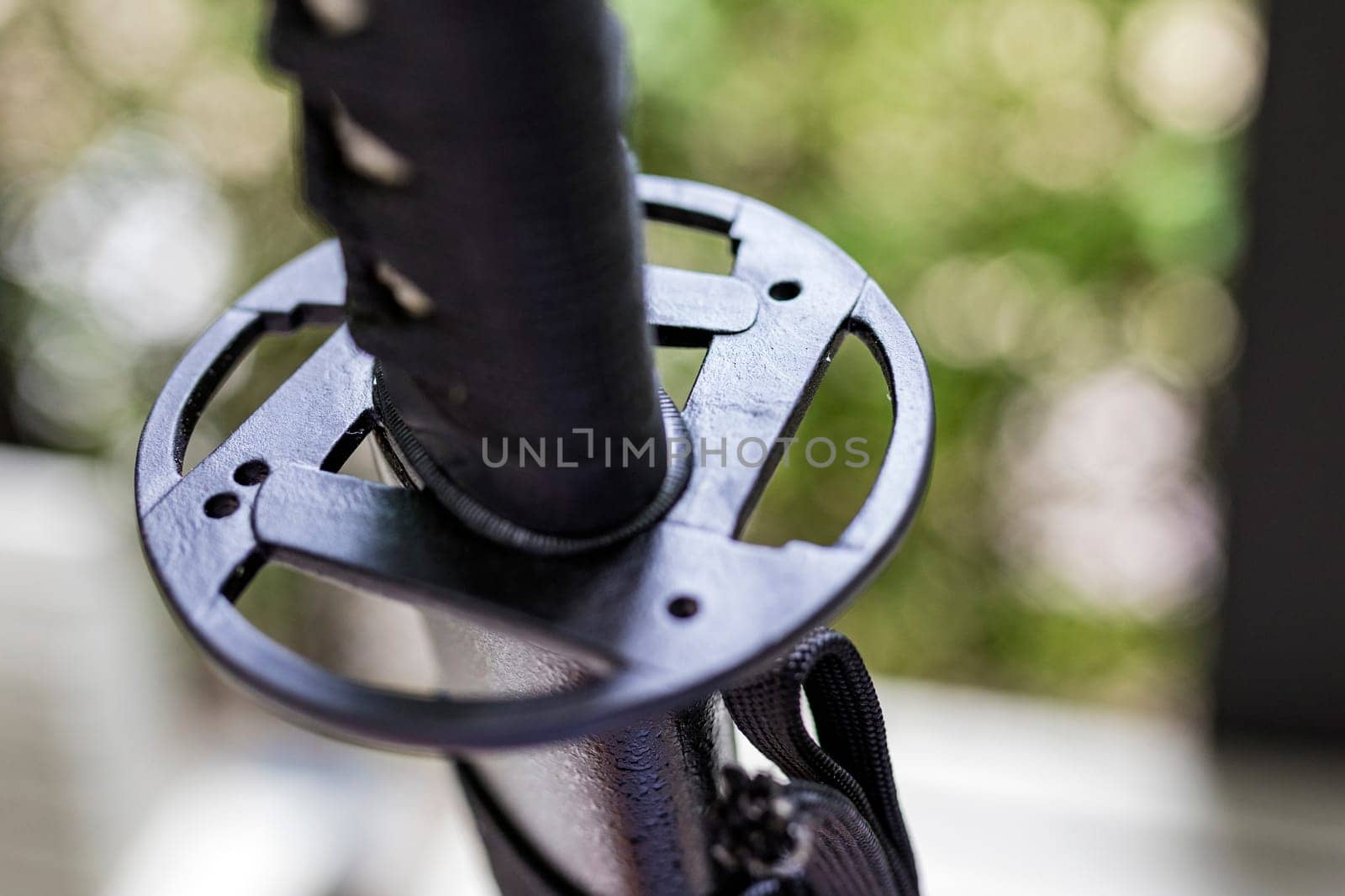 A shallow focus shot of Tsuba, or hand guard, on the handle of a katana (Japanese long sword) It is a work of art that is widely popular and has a high price. The background is a blurred fence line.