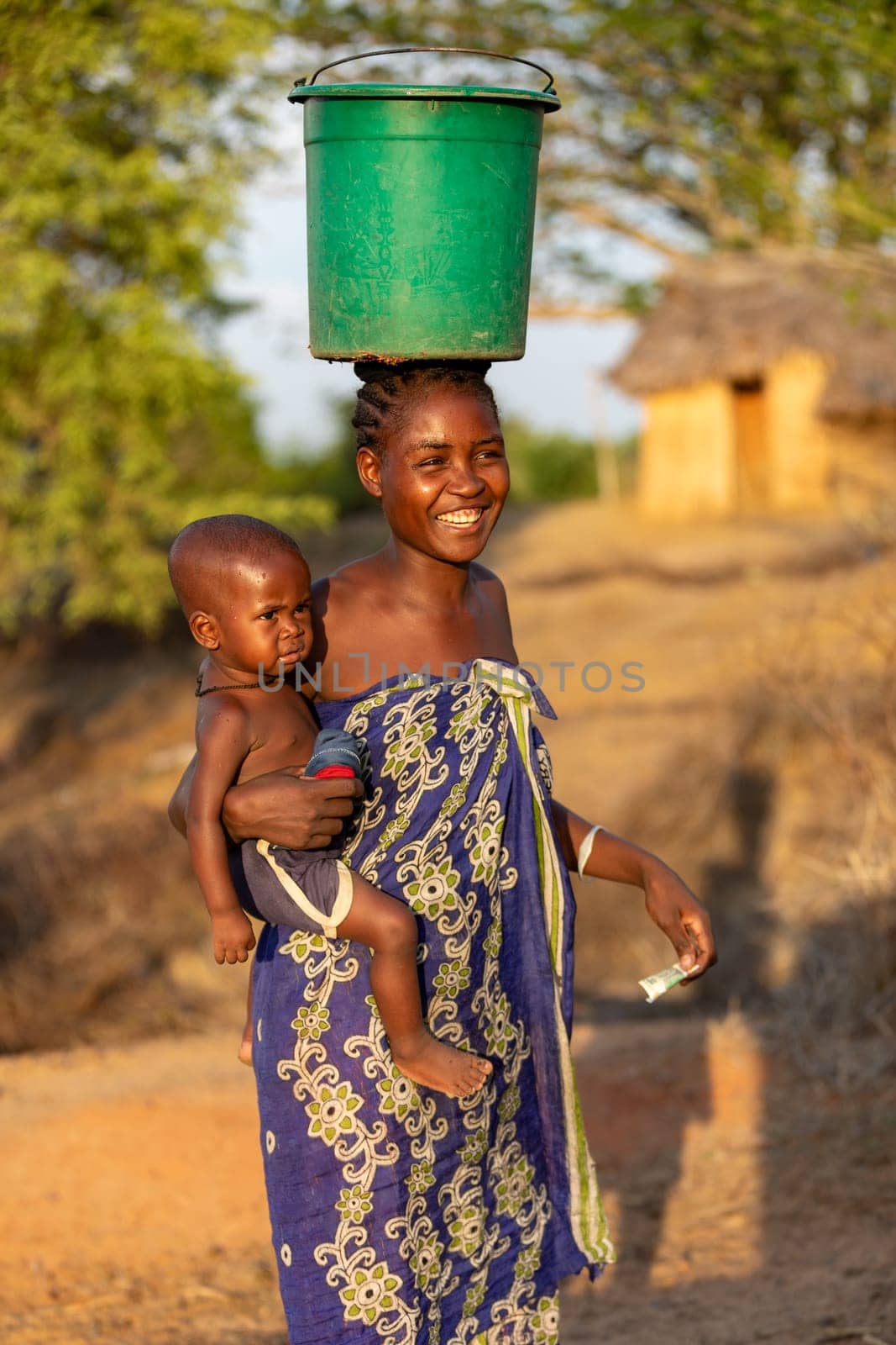 Amkilizato-Mahabo, Madagascar - November 4th 2022: Woman with baby in hand and container on head, a common sight in this rural Madagascar village