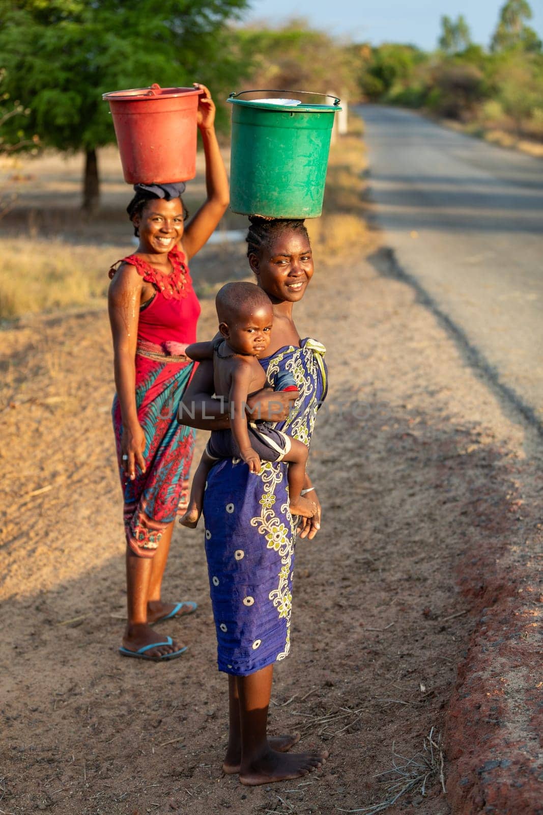 Amkilizato-Mahabo, Madagascar - November 4th 2022: Woman with baby in hand and container on head, a common sight in this rural Madagascar village