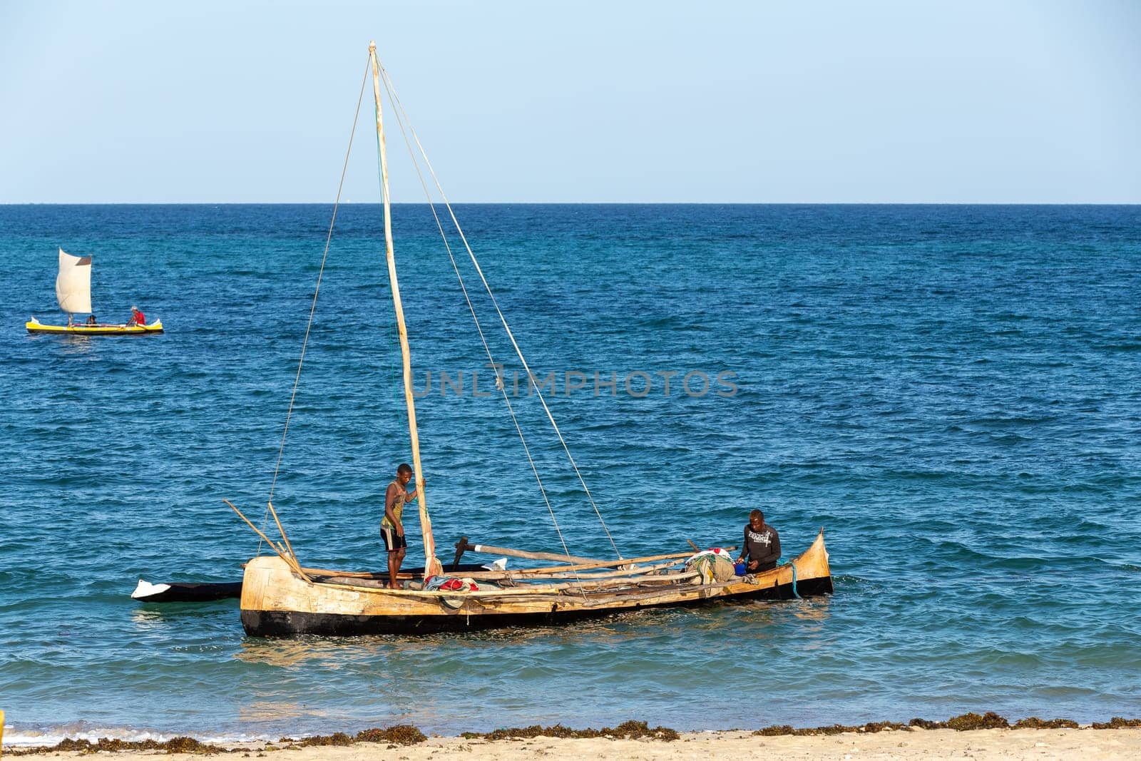 ANAKAO, MADAGASCAR - NOVEMBER 24, 2022: Mans using outrigger canoe carved from tree to transport goods from Toliara to Anakao. Malagasy traditional boat with a single outrigger, is used for centuries.