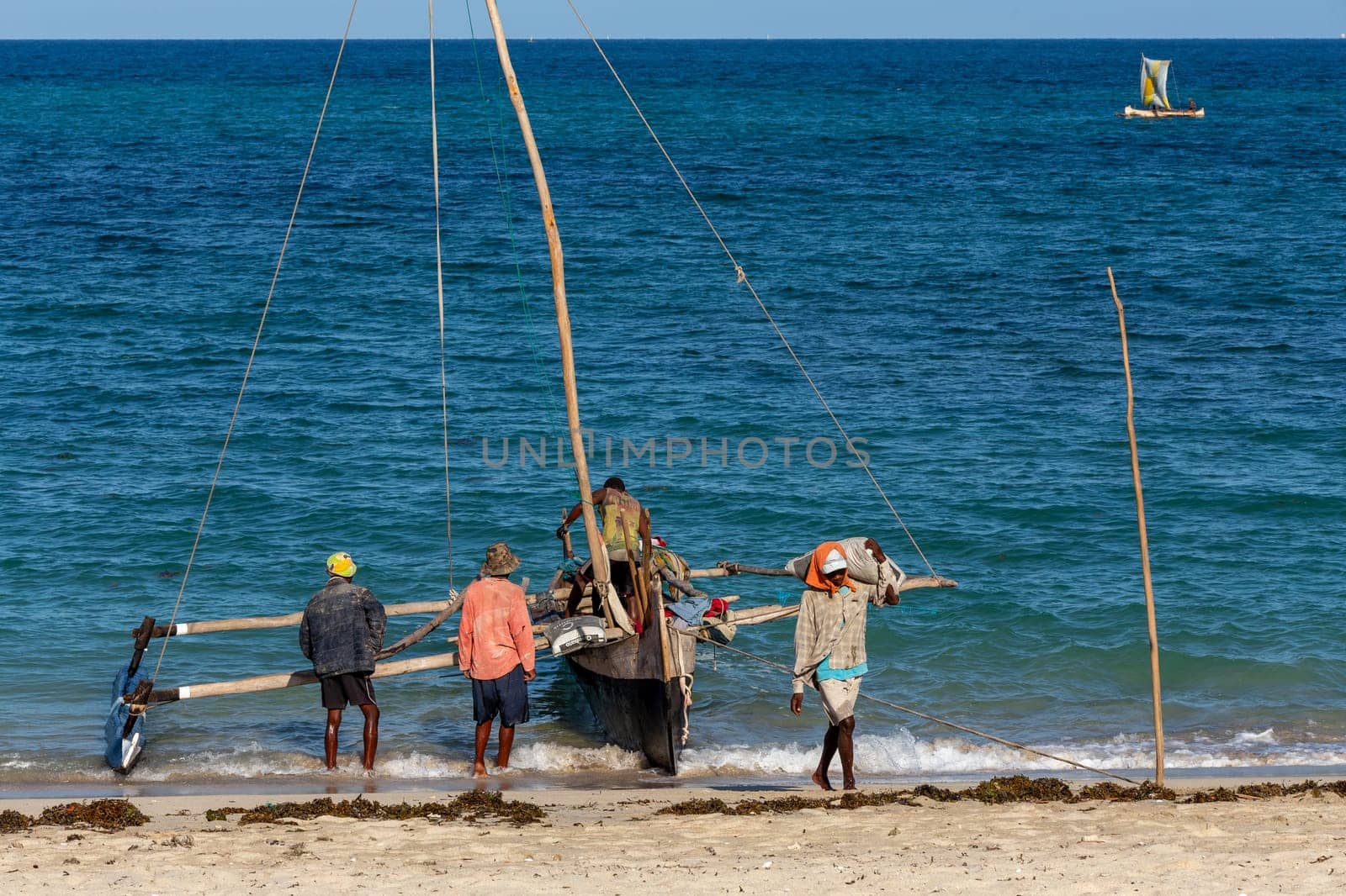 ANAKAO, MADAGASCAR - NOVEMBER 24, 2022: Mans unloading the outrigger carved canoe to transport goods from Toliara to Anakao. Malagasy traditional boat with a single outrigger, is used for centuries.