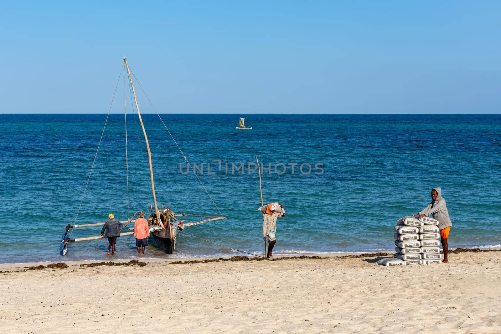 ANAKAO, MADAGASCAR - NOVEMBER 24, 2022: Mans unloading the outrigger carved canoe to transport goods from Toliara to Anakao. Malagasy traditional boat with a single outrigger, is used for centuries.
