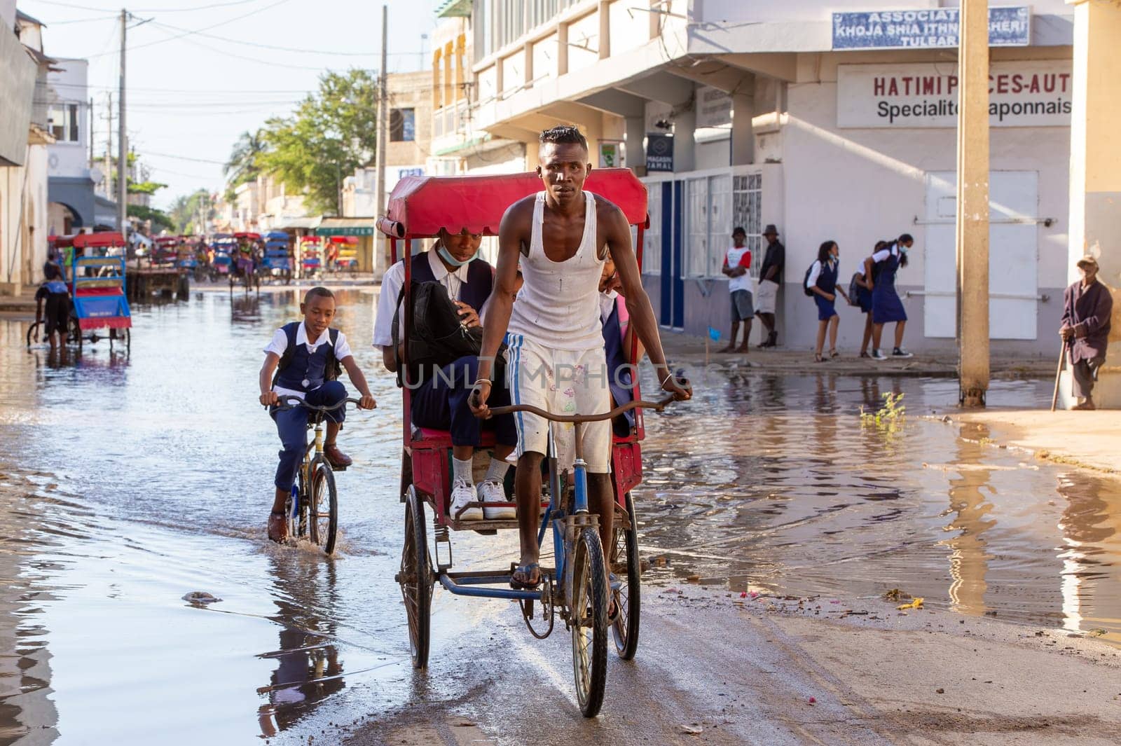 Toliara, Madagascar - November 21. 2022: Traditional rickshaw bicycle with Malagasy passengers on the street, one of the ways to earn money. Everyday life on the cities street of Madagascar.