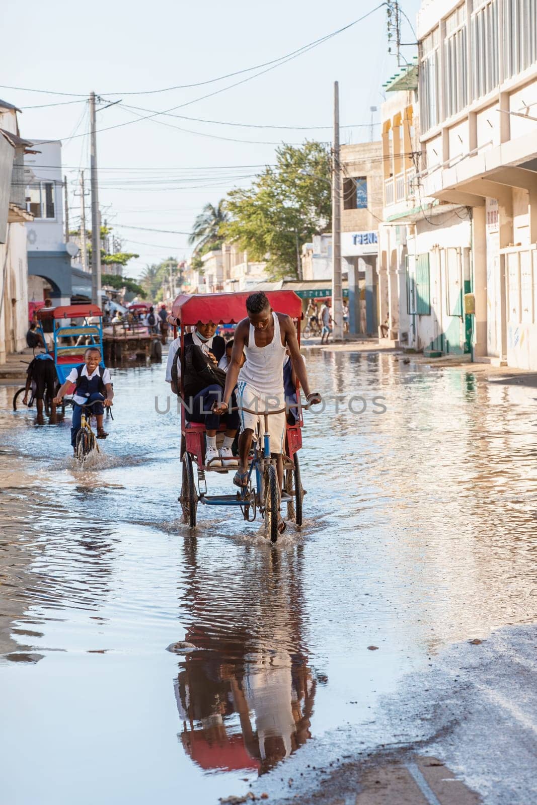 Toliara, Madagascar - November 21. 2022: Traditional rickshaw bicycle with Malagasy passengers on the street, one of the ways to earn money. Everyday life on the cities street of Madagascar.