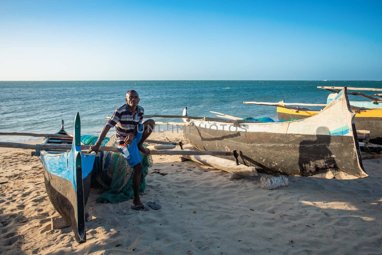 ANAKAO, MADAGASCAR - NOVEMBER 21, 2022: Fishermen resting on traditional outrigger canoe in the coast of Anakao in Madagascar. Malagasy traditional boat with a single outrigger, is used for centuries.