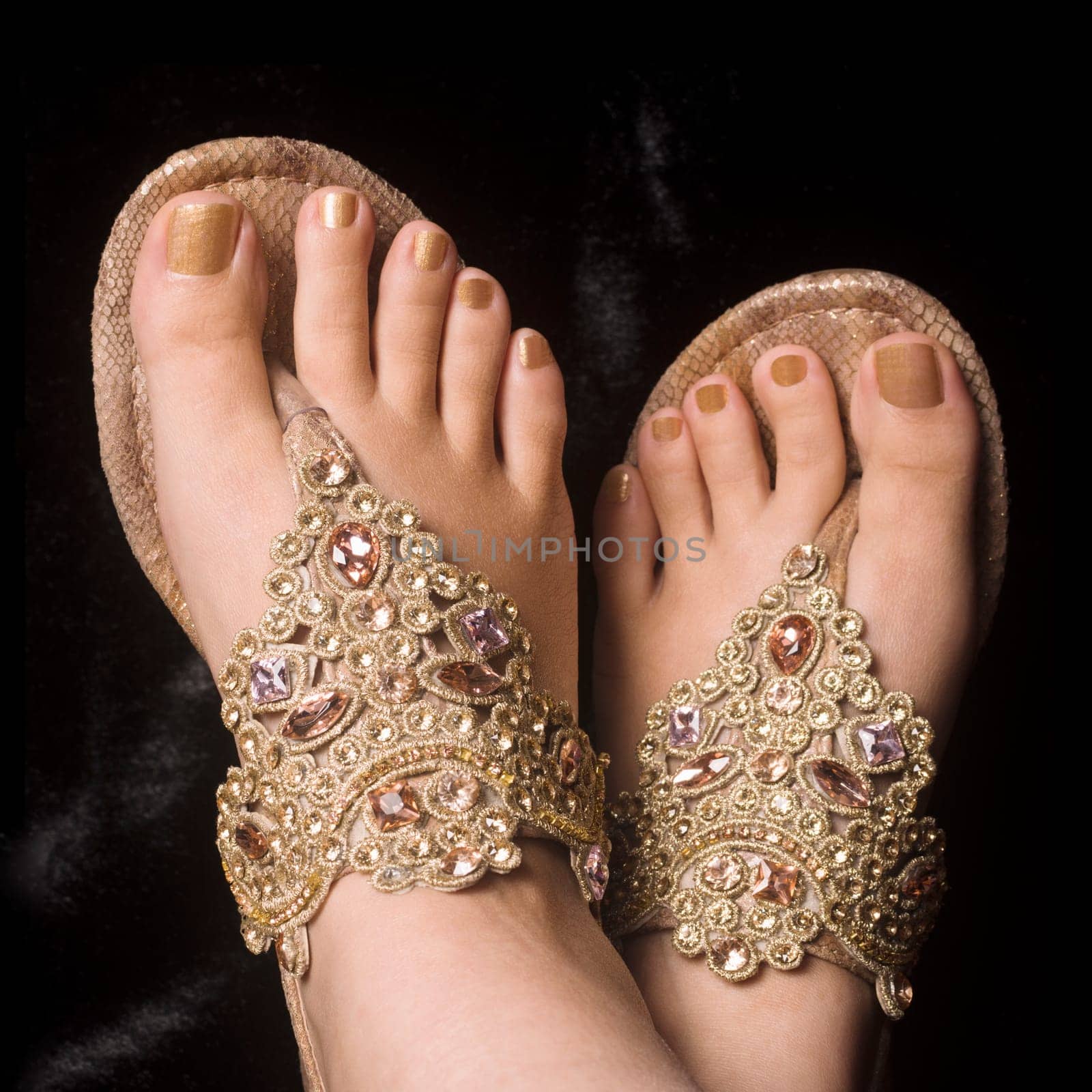 Female legs in elegant gold sandals on black background.