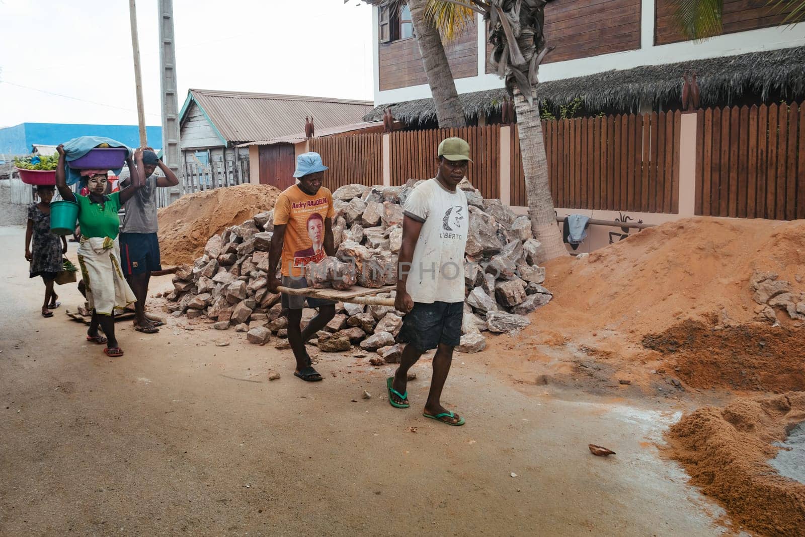 Morondava, Madagascar - November 3rd, 2022: Malagasy men working hard, manually carrying construction stones.