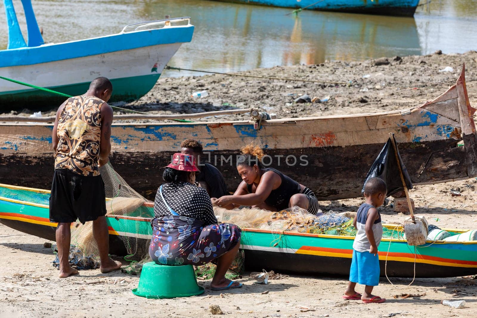 Morondava, Madagascar - November 3, 2022: Fisherman and woman repairing fishing nets at the estuaries of a river, canal Hellot. The woman has a traditionally Malagasy painted face