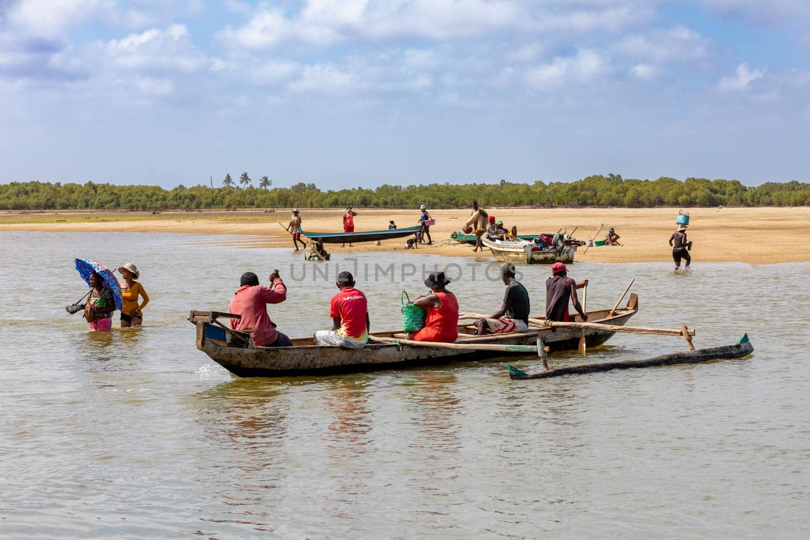 MORONDAVA, MADAGASCAR - NOVEMBER 22, 2022: Malagasy family in traditional wooden boat crossing River in Morondava, Madagascar.