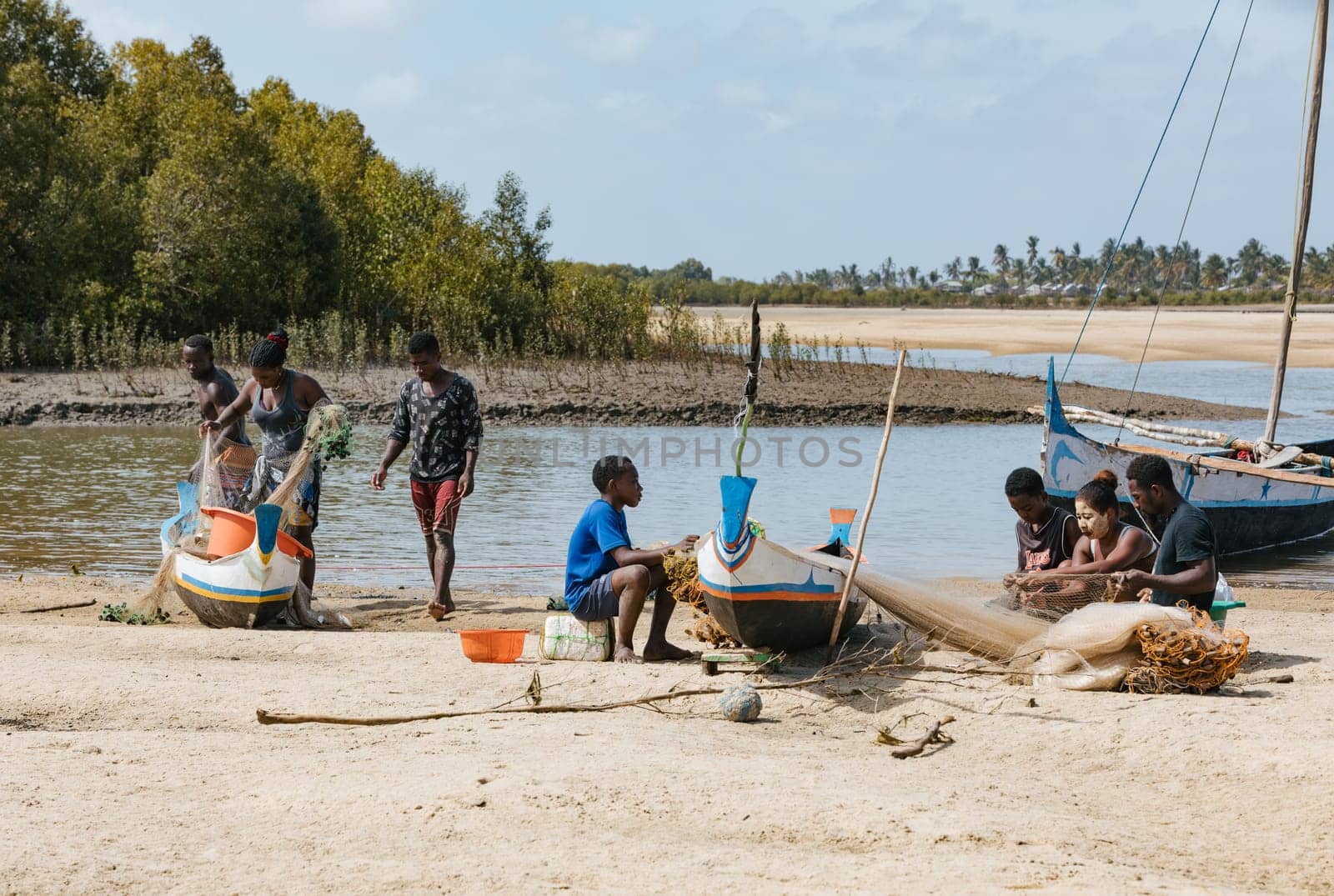 Morondava, Madagascar - November 3, 2022: Fisherman and woman repairing fishing nets at the estuaries of a river, canal Hellot. The woman has a traditionally Malagasy painted face