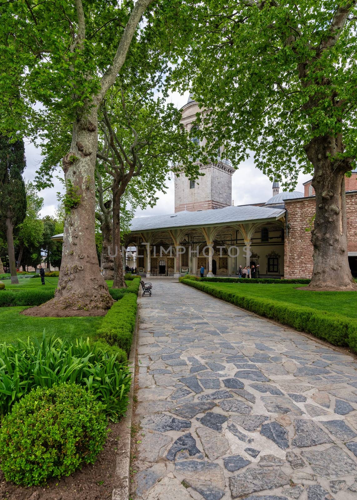 Istanbul, Turkey - May 11, 2023: Stone walkway surrounded by lush trees, leading to the Imperial Council building in the courtyard of Topkapi Palace