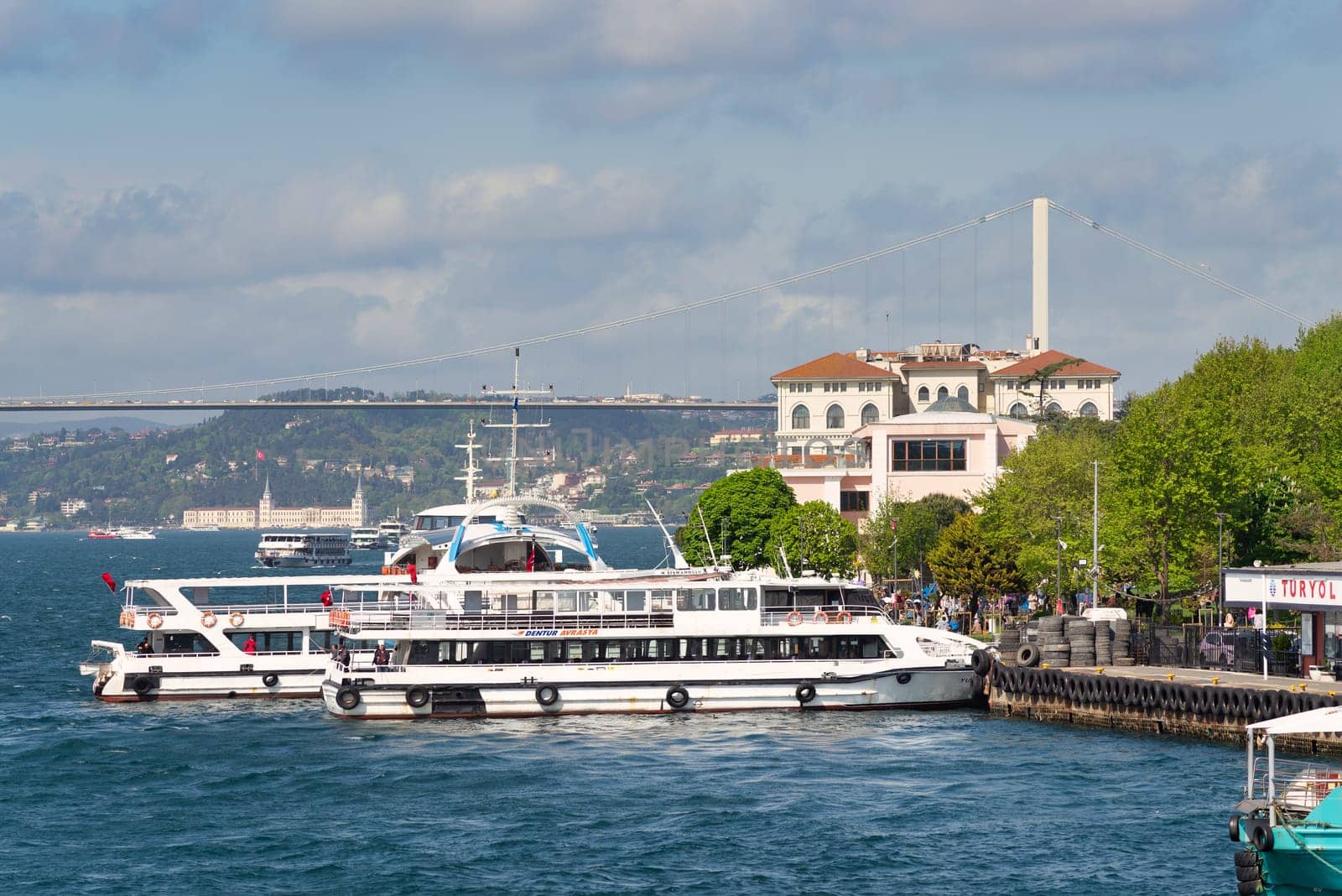 Istanbul, Turkey - May 7, 2023: Dentur Avrasya modern passenger ferry boats docked at Uskudar terminal, with Bosphorus bridge in the background