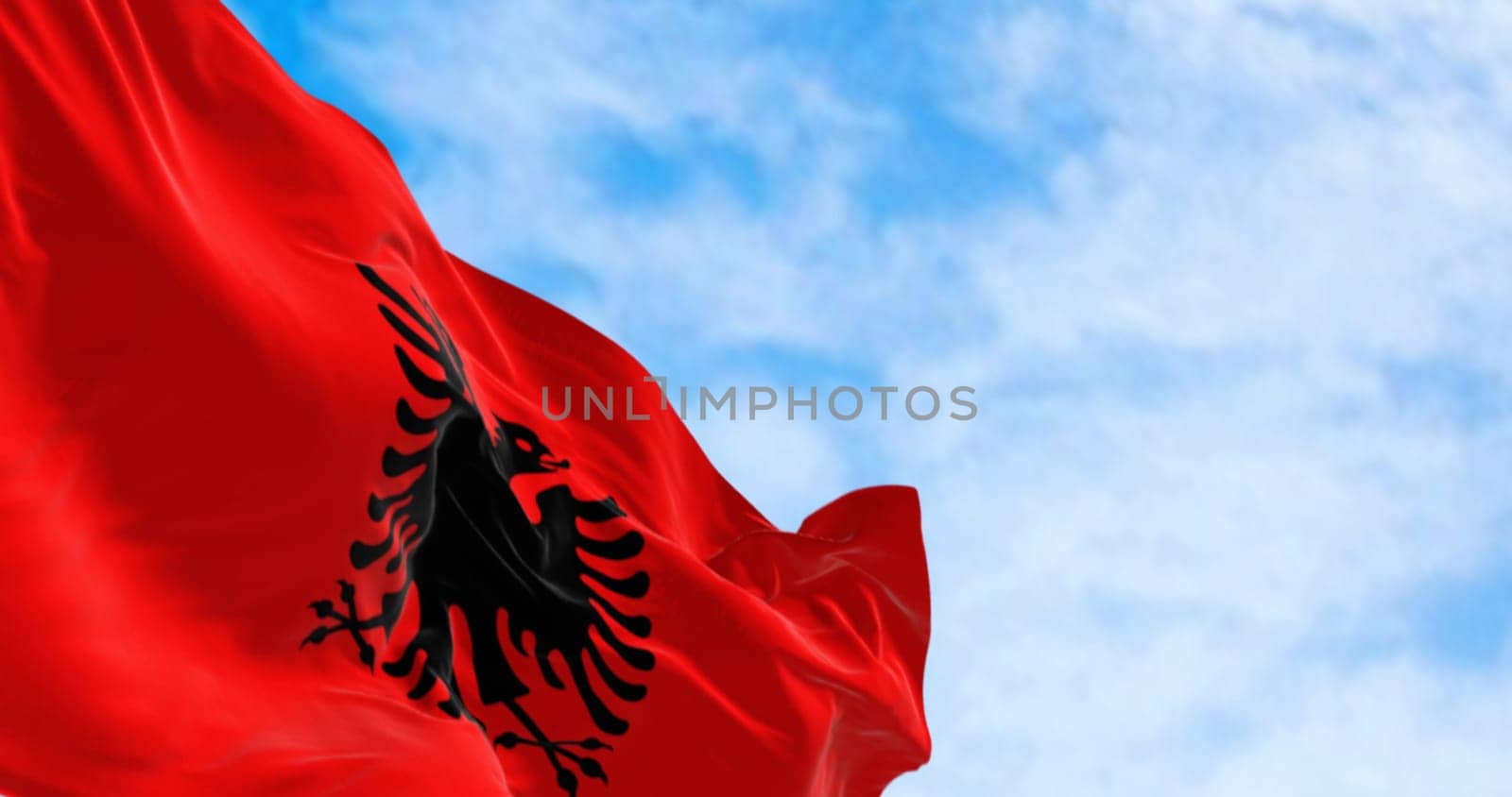 Albanian national flag waving in the wind on a clear day. Red flag with black two-headed eagle. 3d illustration render. Fluttering fabric.