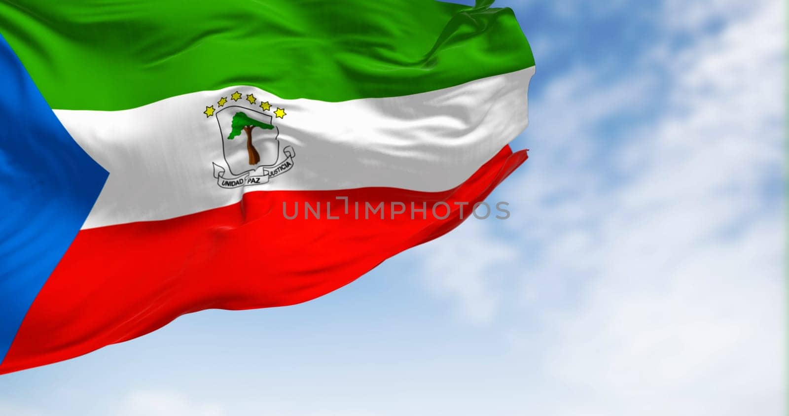 National flag of Equatorial Guinea waving in the wind on a clear day. Horizontal tricolor, with green, white and red stripes and a blue triangle at the hoist. 3d illustration render. Selective focus