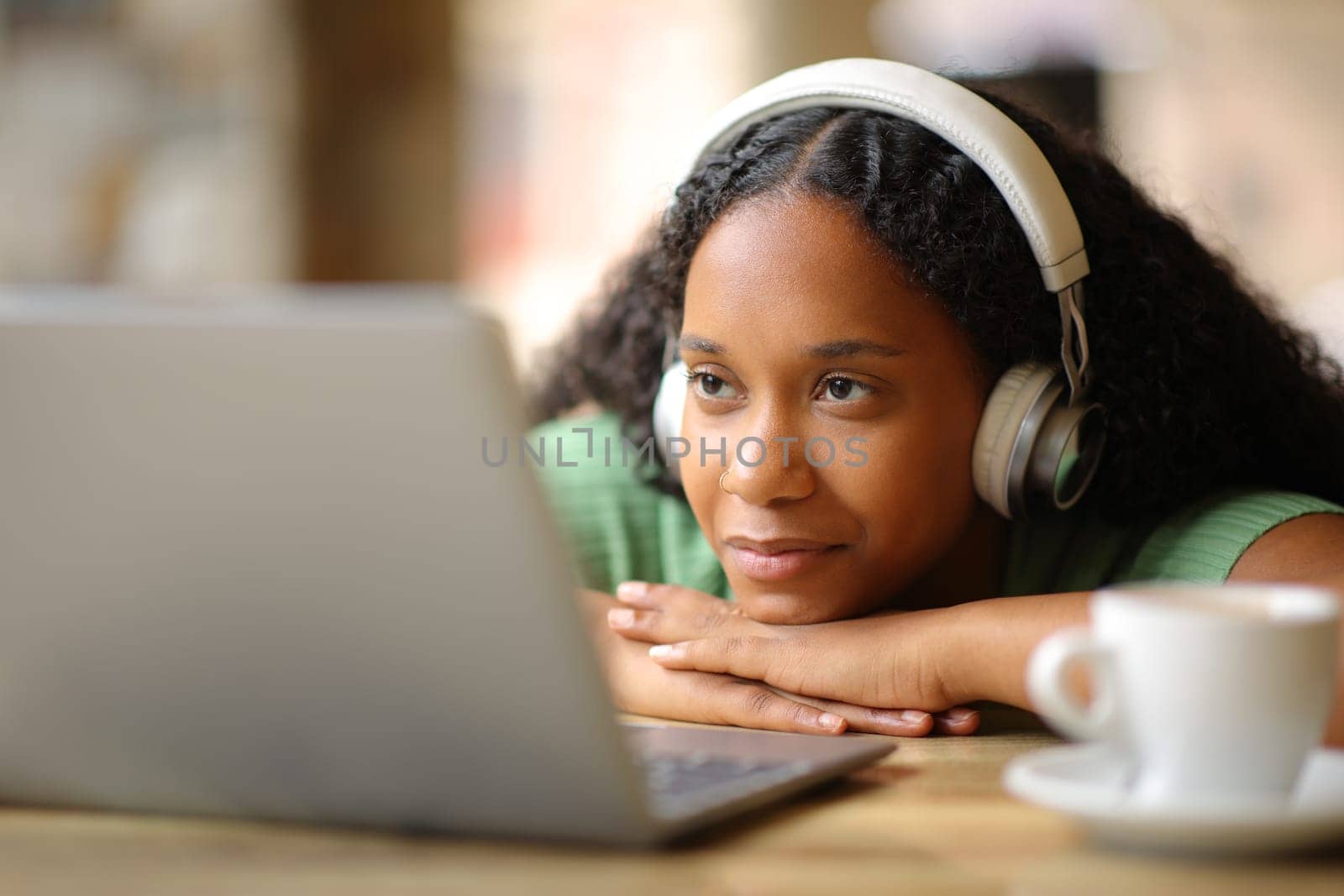 Black woman wearing headphone watching media on laptop in a restaurant terrace
