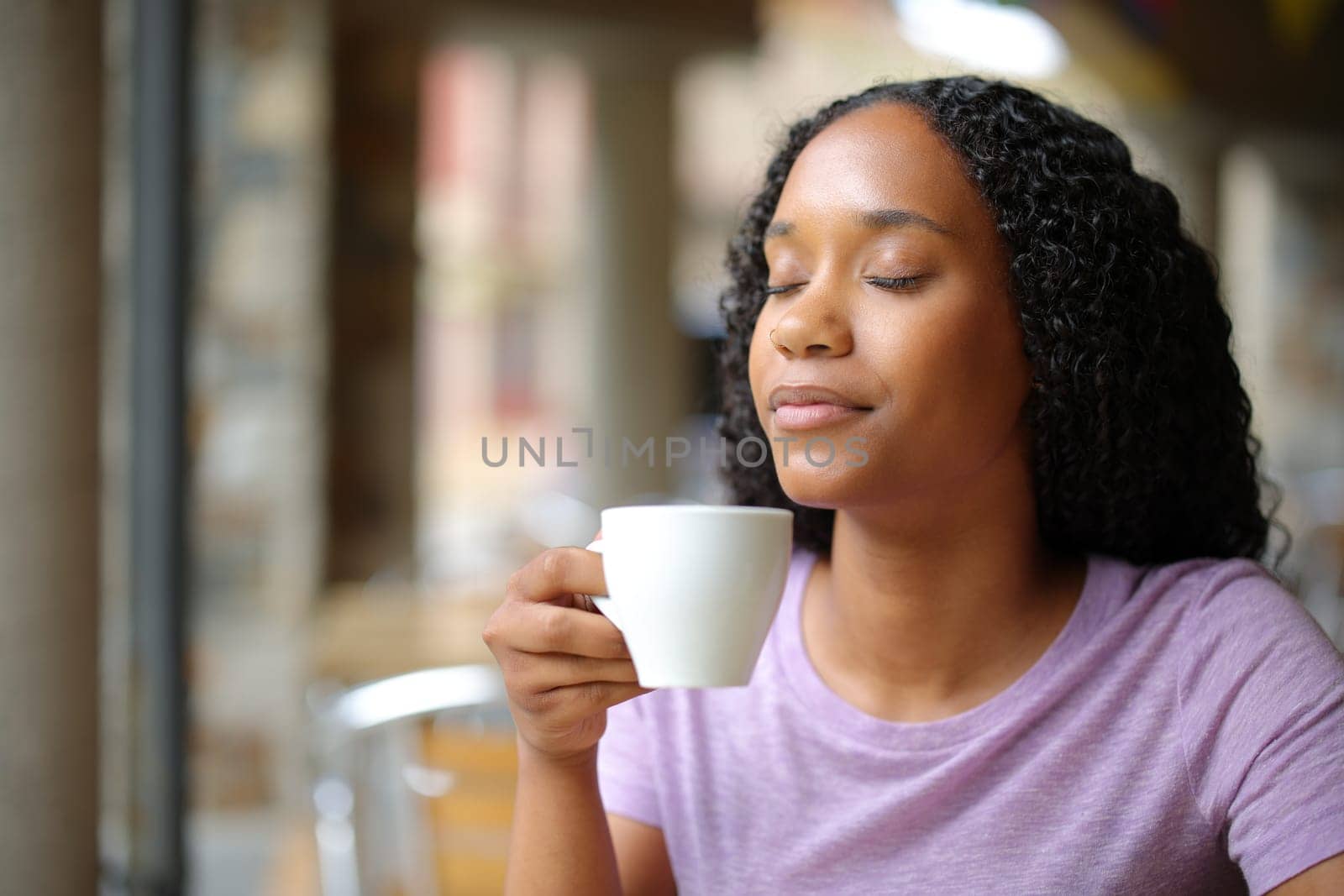 Black woman enjoying of a coffee cup smelling deeply in a restaurant terrace