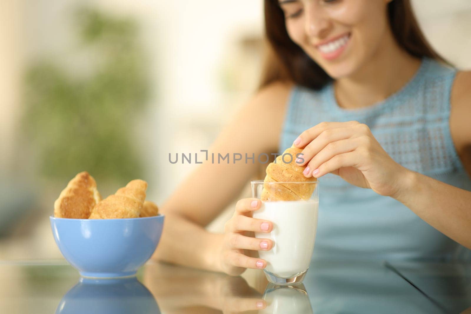 Happy woman dipping croissant in milk glass at home