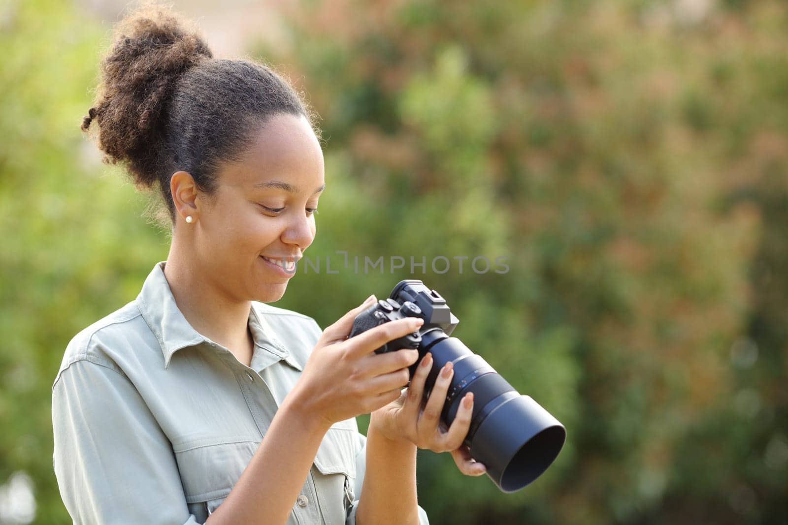 Happy black photographer checking mirrorless camera in a park