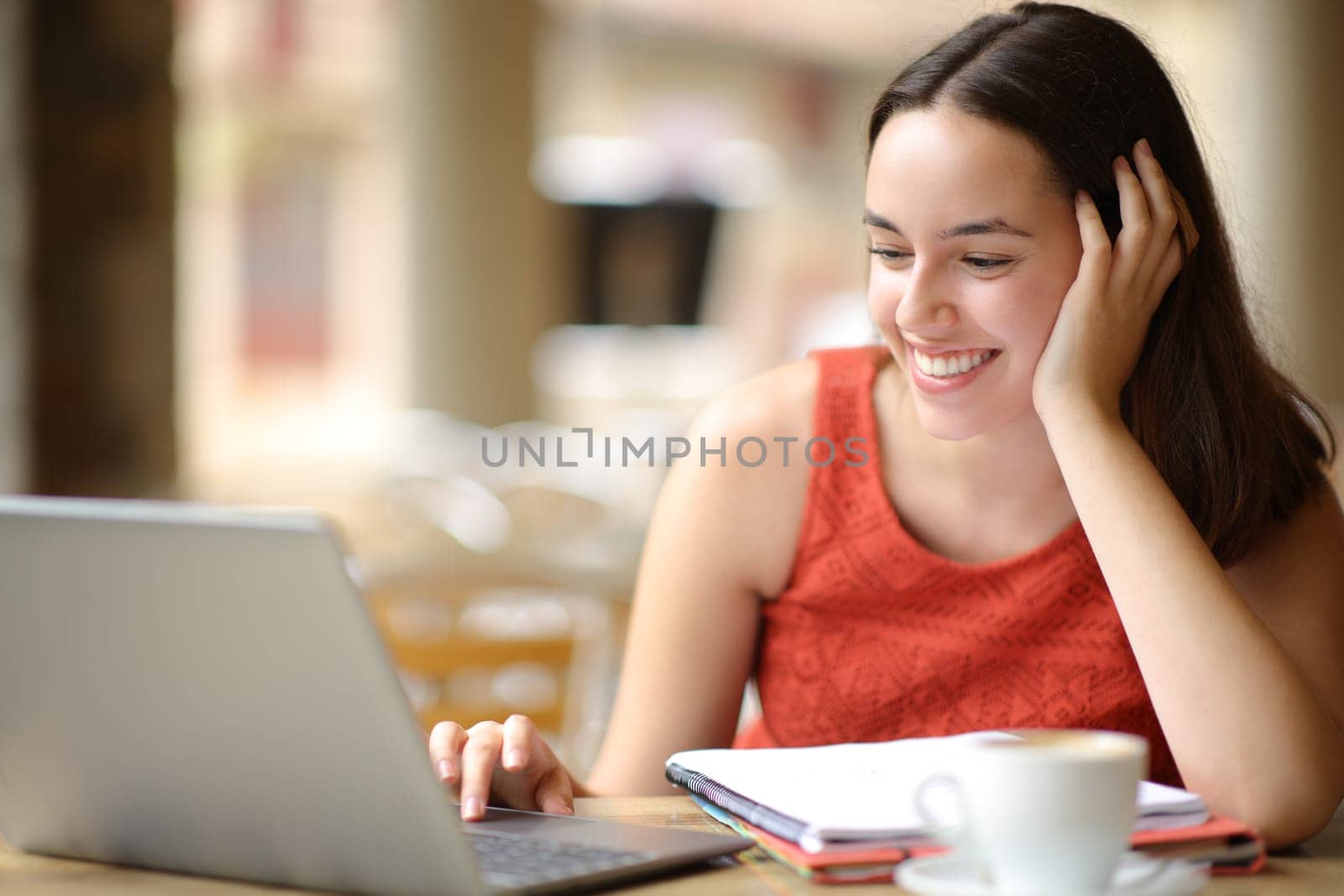 Happy student elearning using laptop in a bar terrace