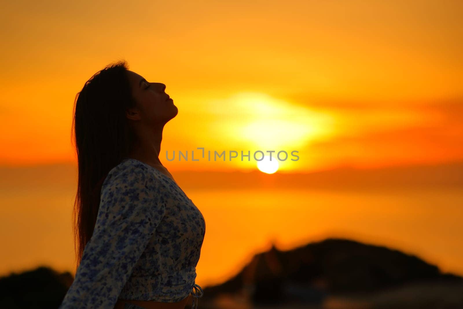 Side view silhouette of a woman breathing fresh air in the coast at sunset