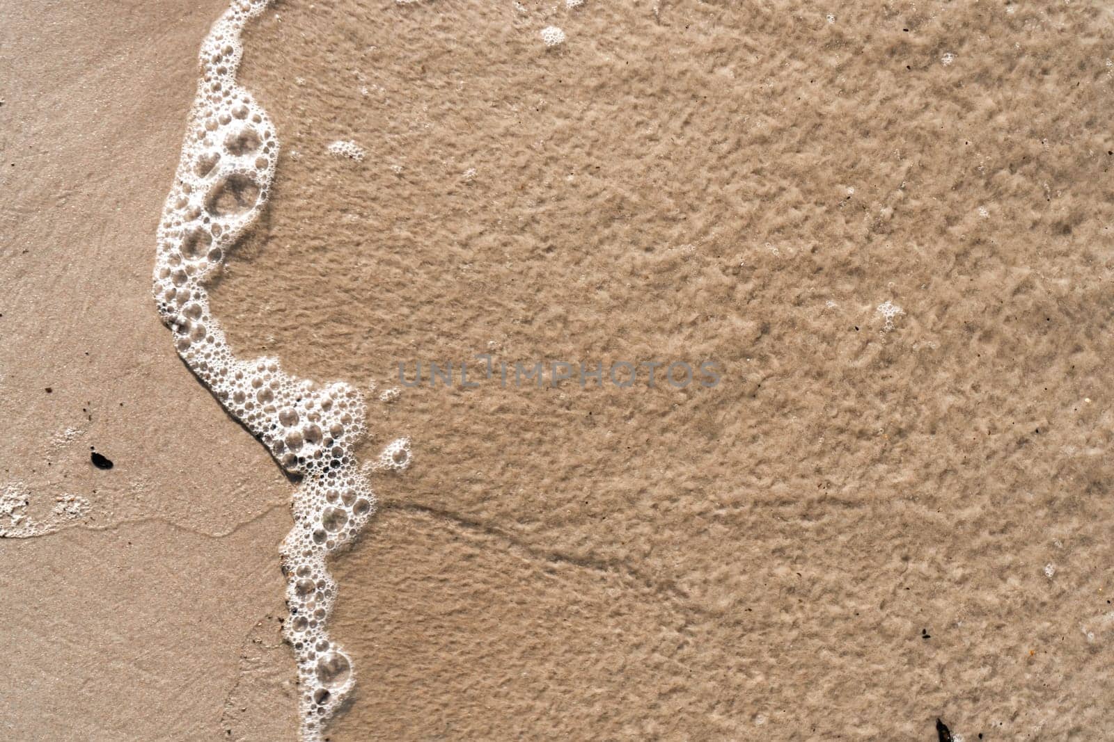Top view of clear foamy water of sea ocean. Yellow golden clean sand seen through water. Beach, summer, holidays, seascape, vacation, coastline, seashore, seaside, travelling, tourism, wallpaper.