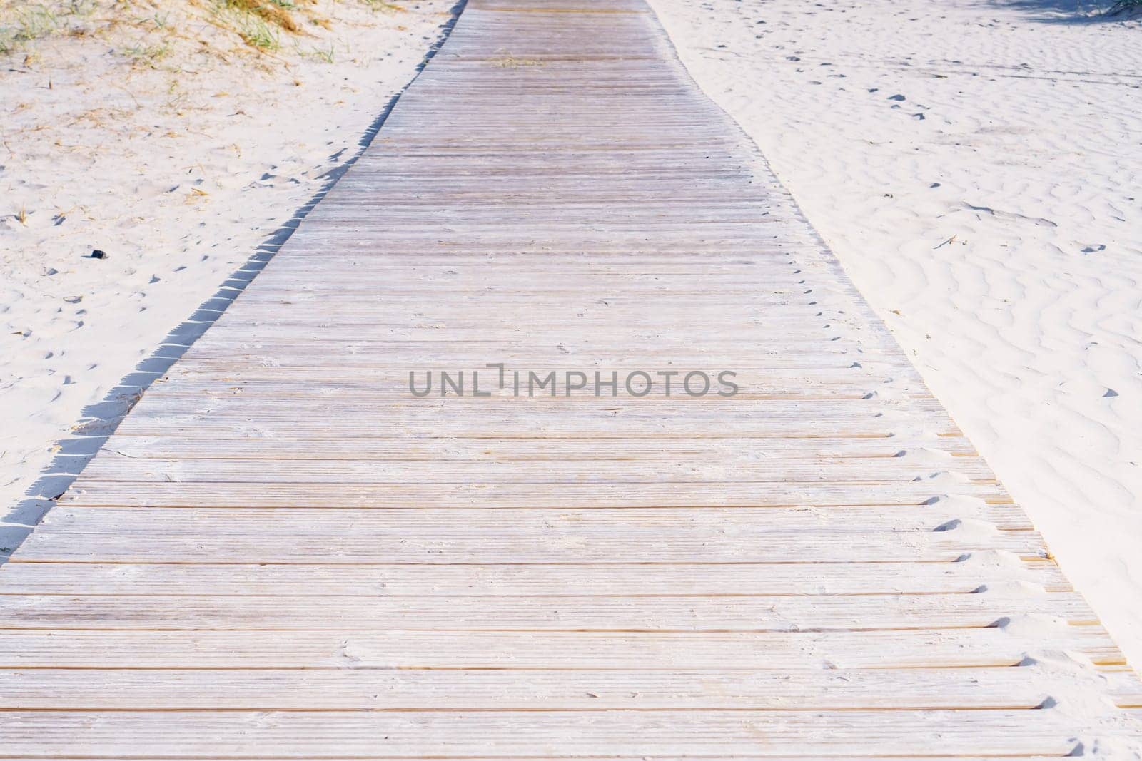 Wooden pathway road boardwalk surrounded by sand with footprints to beach sea ocean on sunny summer day. Summertime, holiday, vacation, travelling, nature, landscape, seashore, coastline, tourism.