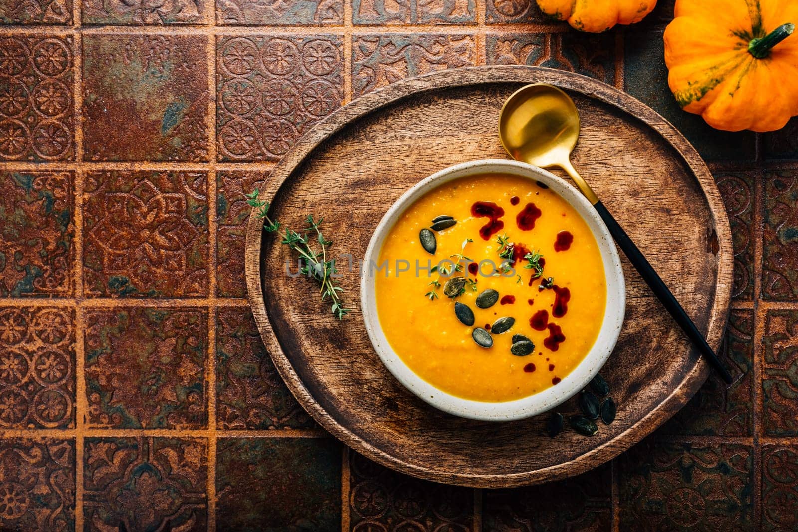 Pumpkin soup with pumpkin seeds  and pumpkin seed oil served in bowl on rustic kitchen table