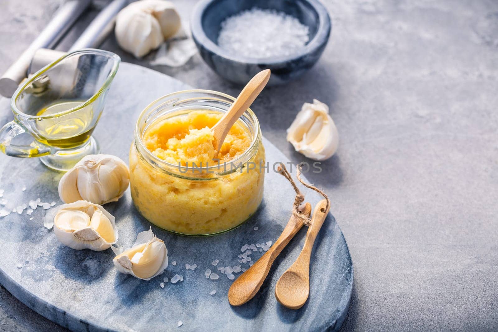 Homemade garlic paste in a jar with peeled garlic, salt, crusher and garlic heads, with copy space