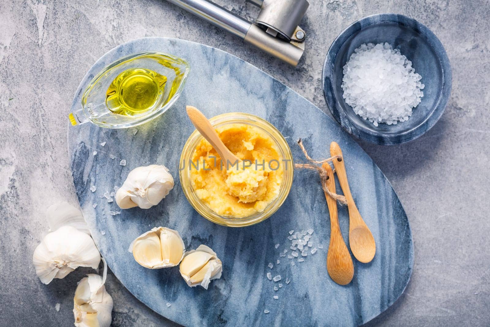 Homemade garlic paste in a jar with peeled garlic, salt, crusher and garlic heads.
