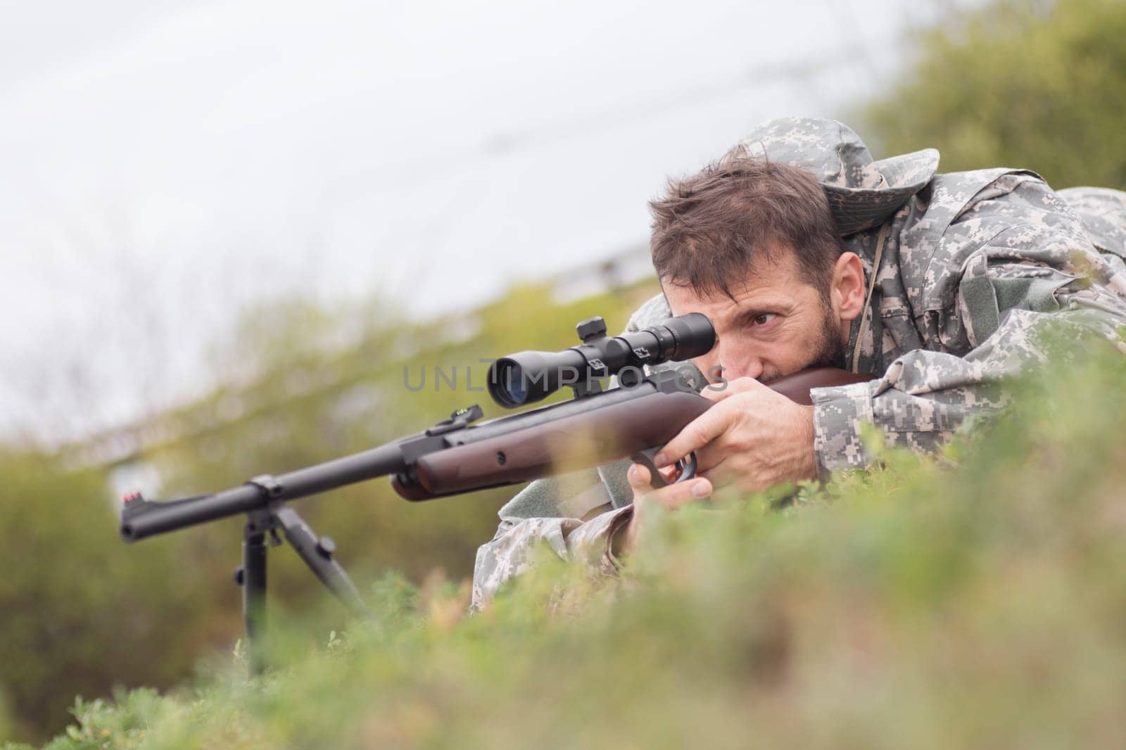 The hunter or army soldier in military uniform is aiming and shooting a weapon with sniper.