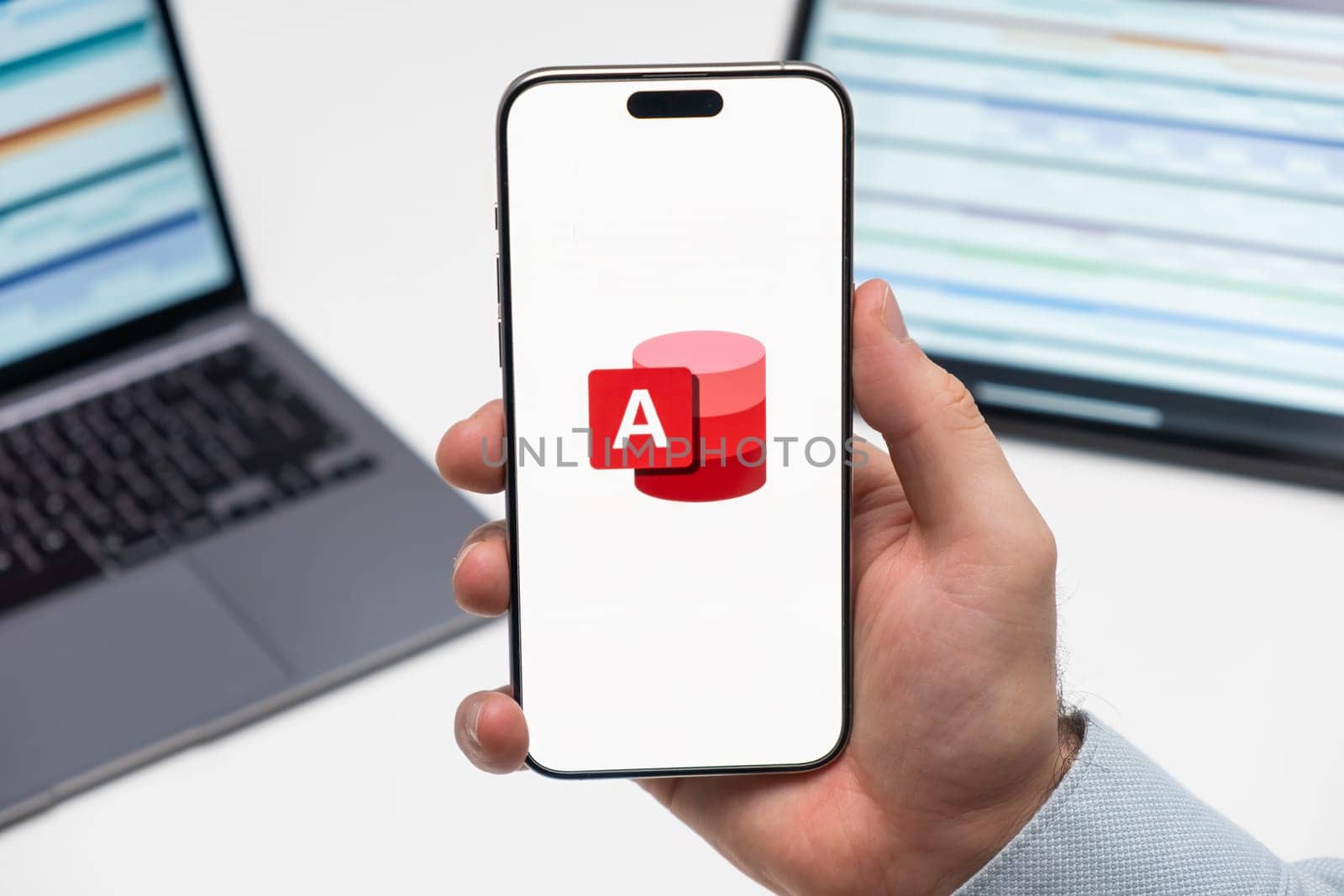 PRAGUE, CZECHIA - JULY, 2024: Access logo on the screen of smartphone in mans hand and laptop on the background